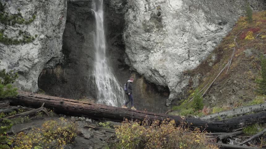 A woman hikes past a waterfall