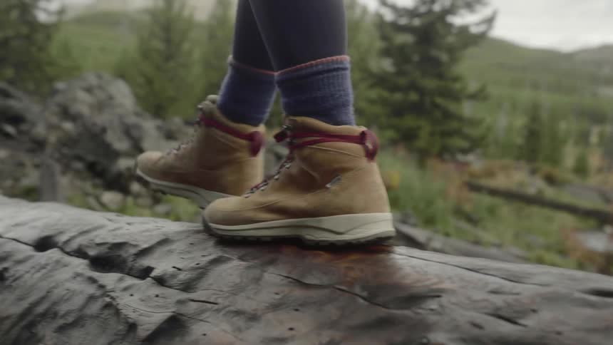Woman in hiking boots walks across log over stream