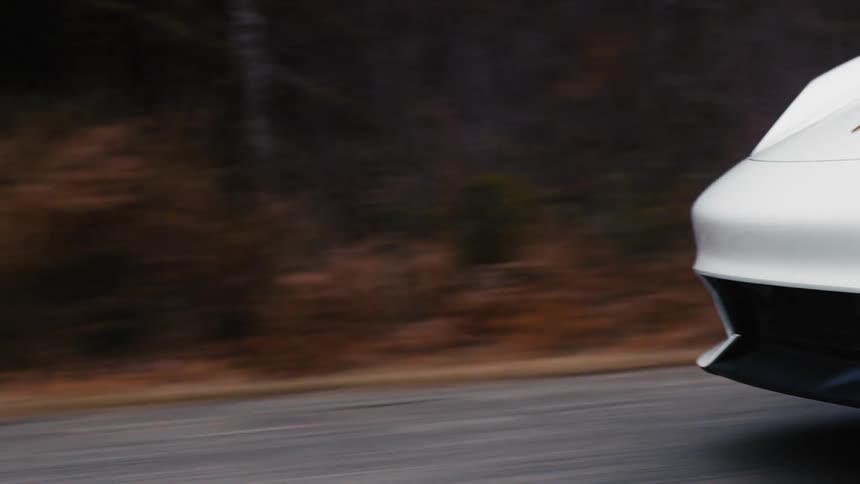 A white sports car travels on a rural road