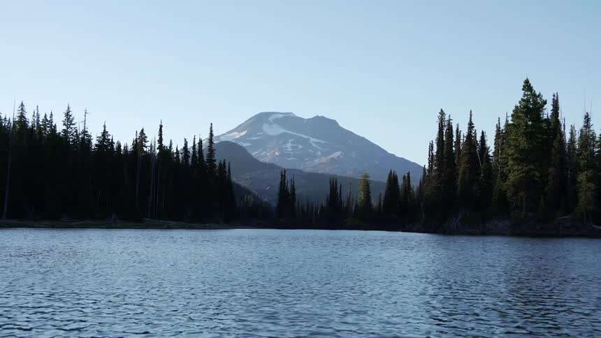 A lake surrounded by a fir forest sits with a mountain in the distance