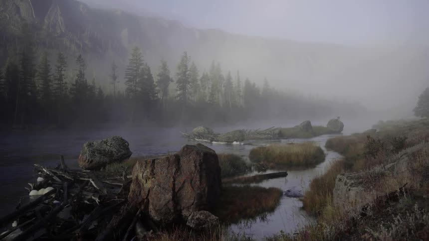 Fog hangs over a river running around small rocky islands