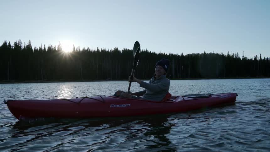 A woman kayaking in a lake with trees in the background