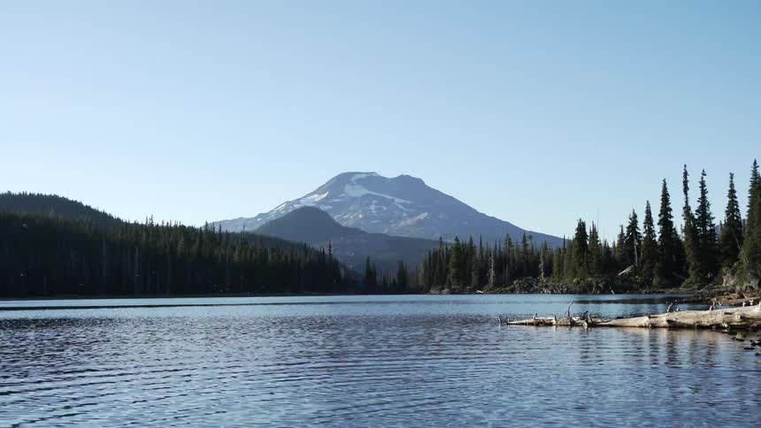 Calm lake waters near forest in front of mountain at day