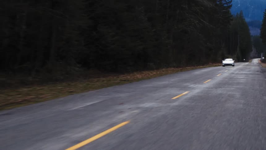 Vehicles travel on the long road past the forest
