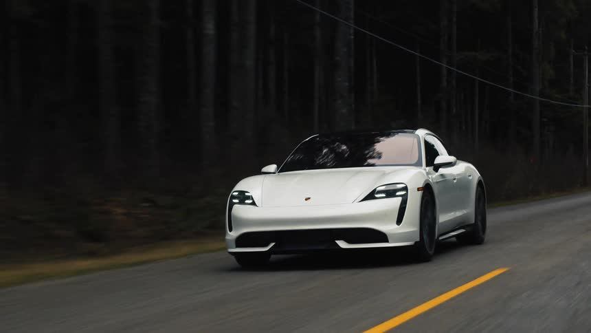 White porsche taycan driving on road through forest