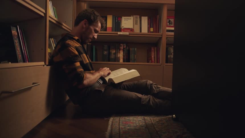 A man sits on the floor and flips through a book