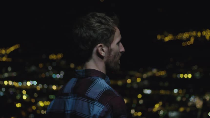 A man stands and looks out at the city skyline at night
