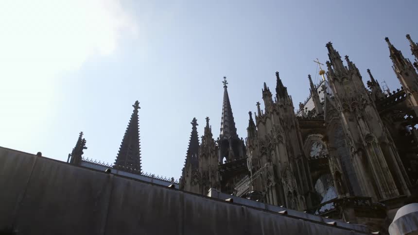 A cross sits on top of an ornate historical church with several eaves