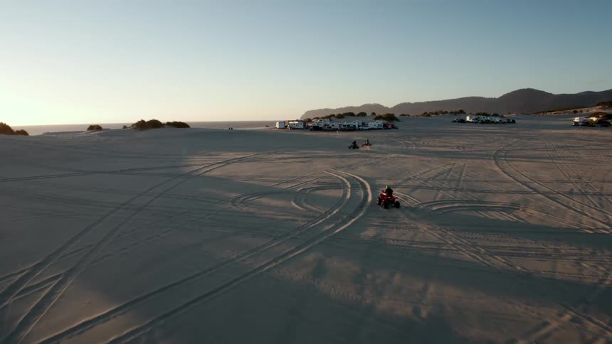 Quad bikes riding on the sand of a beach at sunset next to the mountains