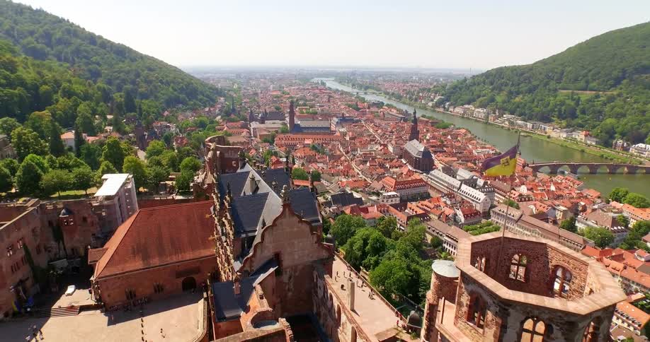 A river runs through a quaint town located at the base of tree covered hills