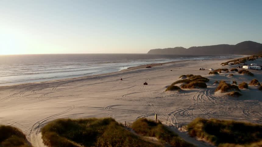 People ride atvs on the beach sand leaving tracks on a sunny day