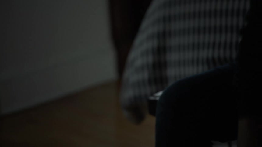 A white man sits in a bedroom and puts on a boot