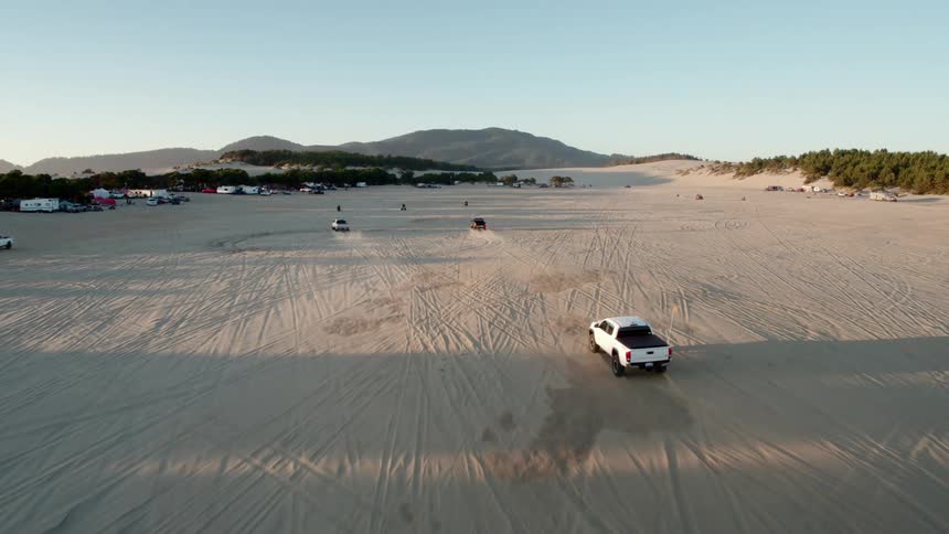 Trucks race through desert past forest toward mountains