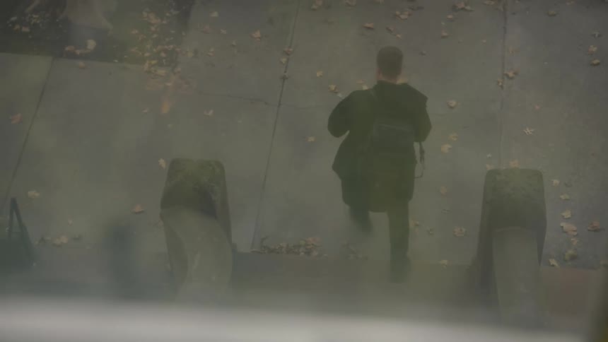 A teenage boy walks down the stairs of a building and swings his backpack onto his shoulder