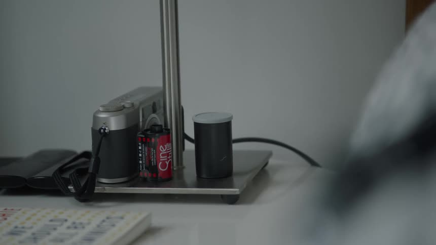 A camera and a roll of film sit on a lamp base on a table