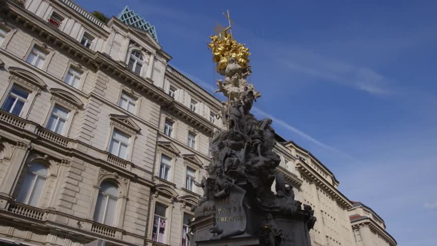 An ornate gold topped statue sits between historical buildings