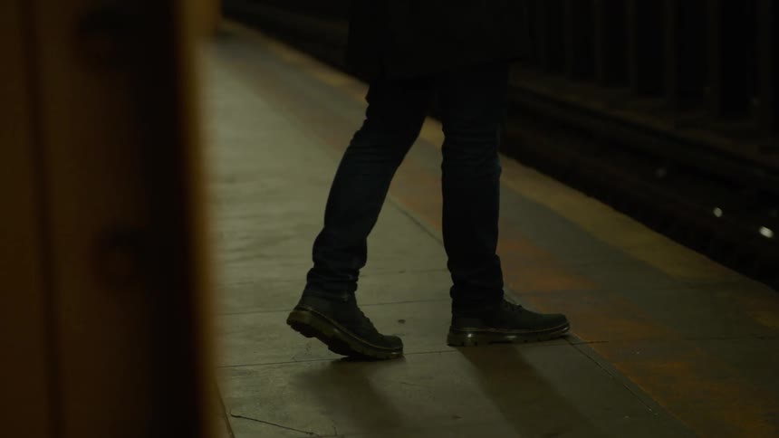 Male waiting for the subway train walks onto the yellow painted caution line at the edge of the platform