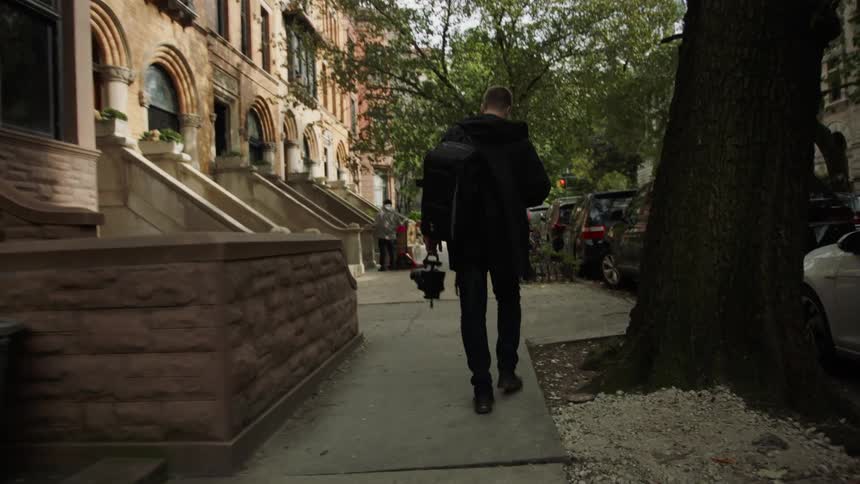 A man with a camera walking a neighborhood with brownstones