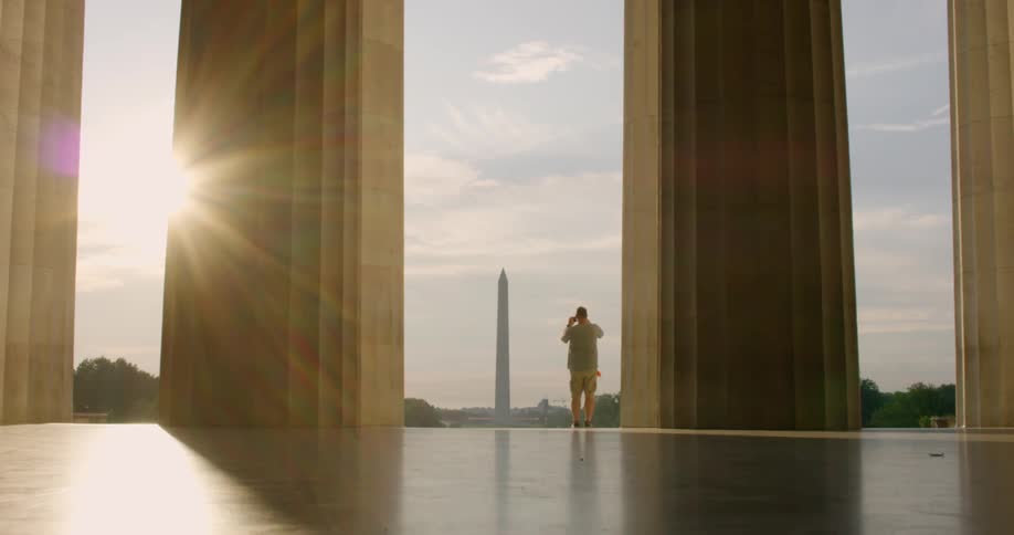 A man talking photographs of the washington monument from the front of a nearby building