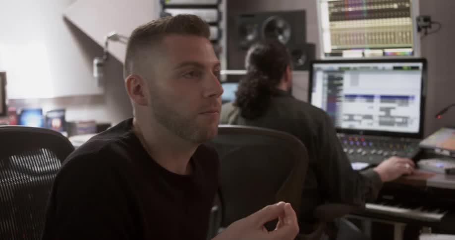 Two men in a recording studio talk and work on equipment
