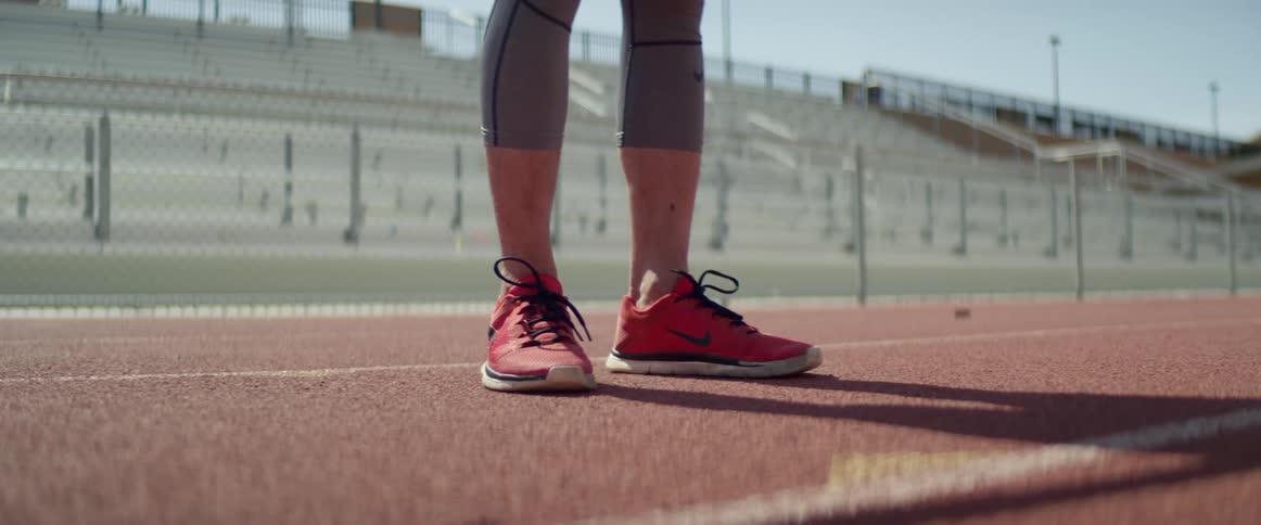 A person wearing red running shoes is widening their stance while standing on a running track