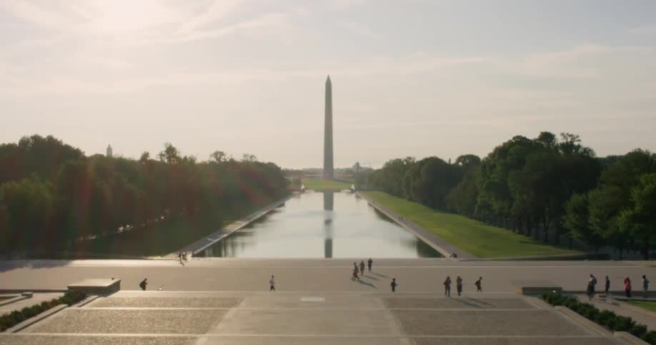 People walk on the sidewalk by a large national monument