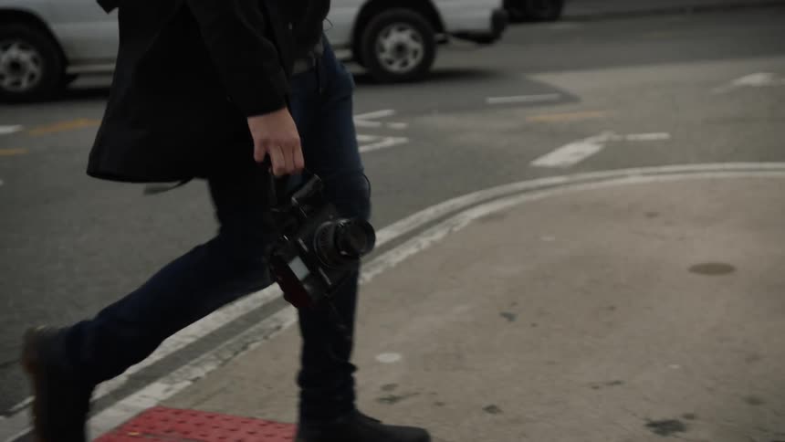 A man is walking in a city and holding a camera