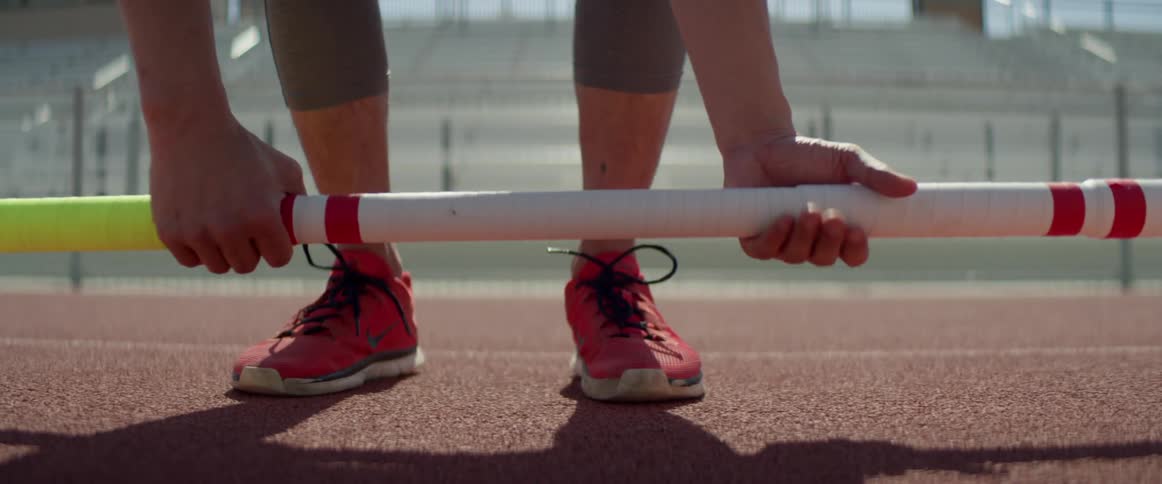 An athlete picks up a colored pole in a track stadium