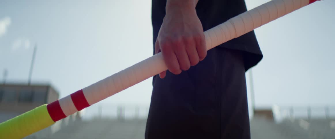 A man stretches as he holds a pole vault on a track