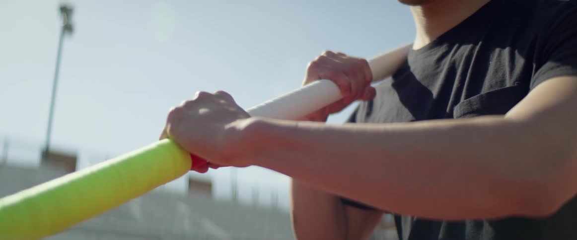 A pole vaulter tightens his grip on the pole while standing in an empty stadium