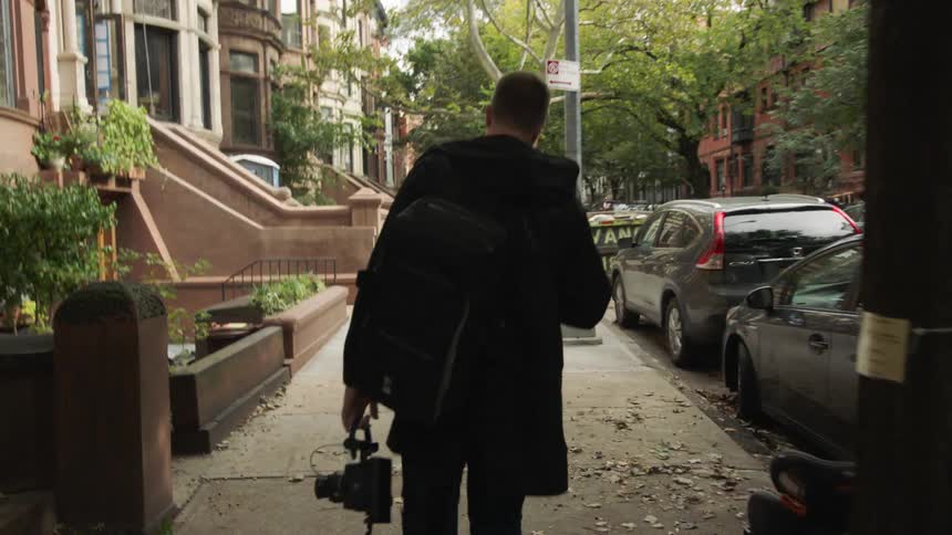 Man carrying photography equipment walks down neighborhood street