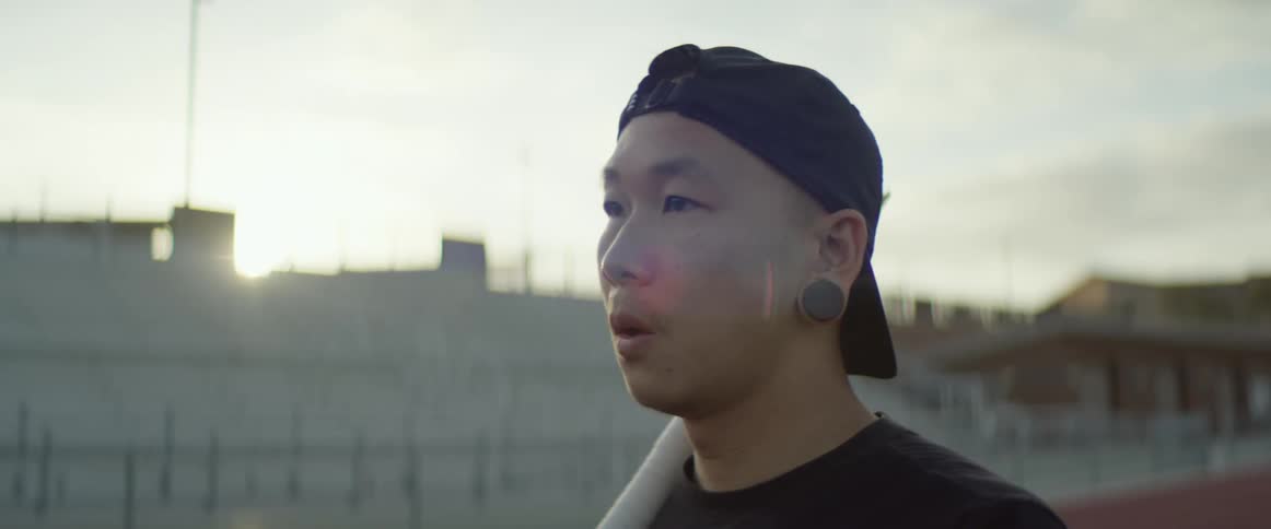 Young asian man stands on the tracks of a stadium at sunset