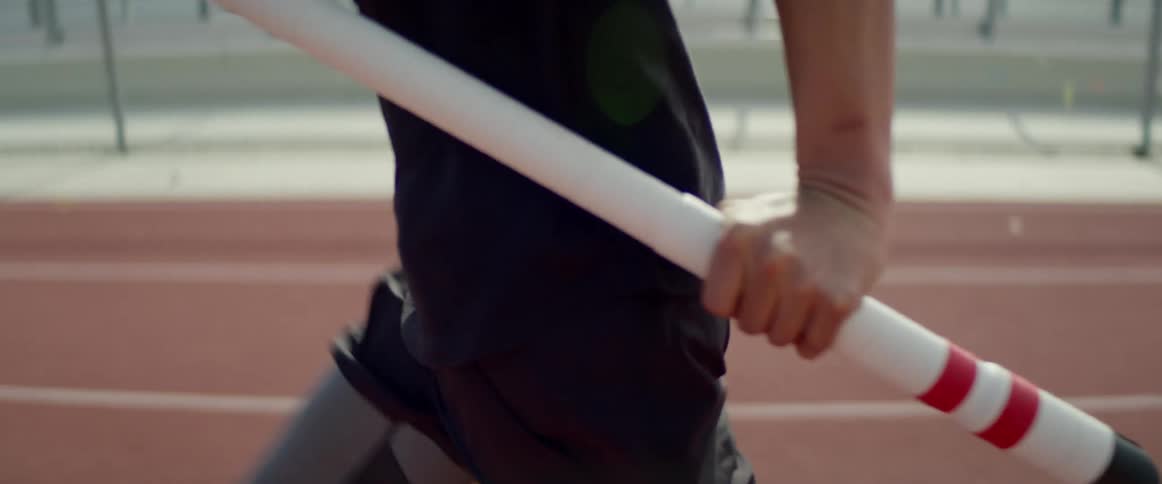 A teenager carrying a pole runs along a track