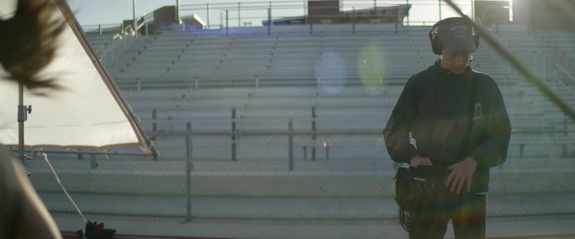 Film crew follows woman running in sports arena while filming