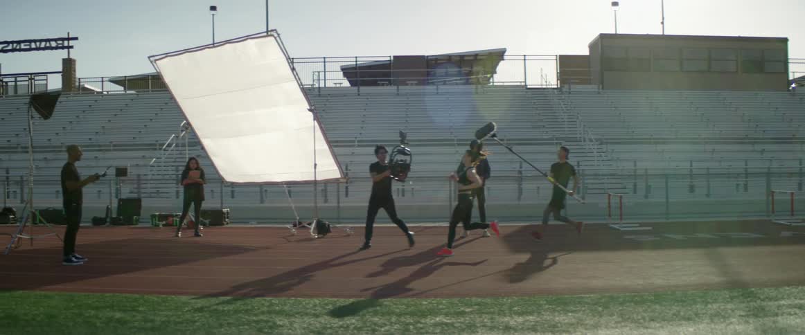 A film crew records a female athlete running along a race track