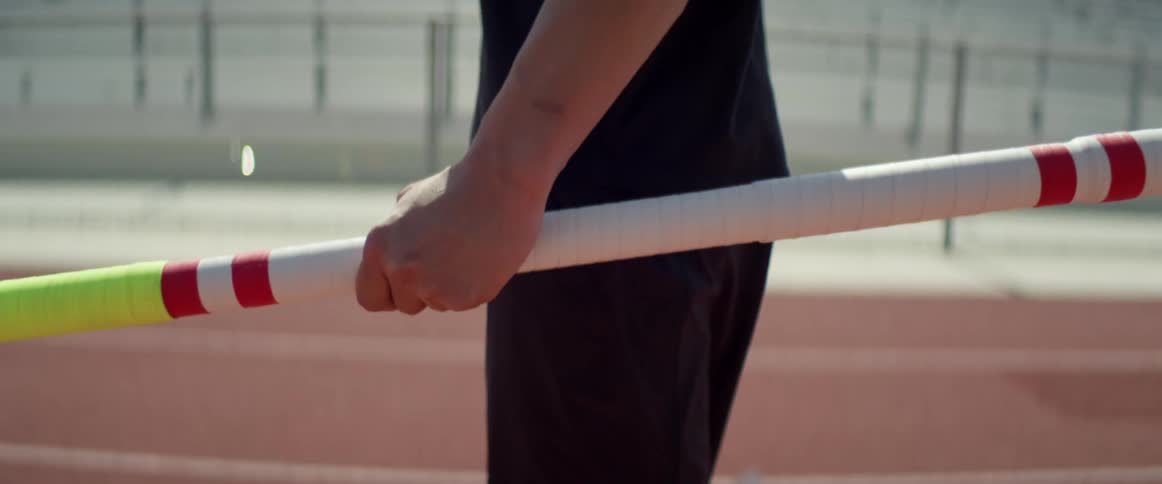 A white male athlete stands on a race track holding a pole