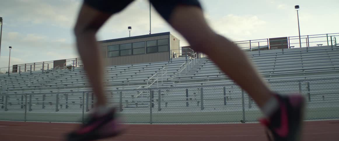 Men in shorts run on a track in an empty stadium on sunny day
