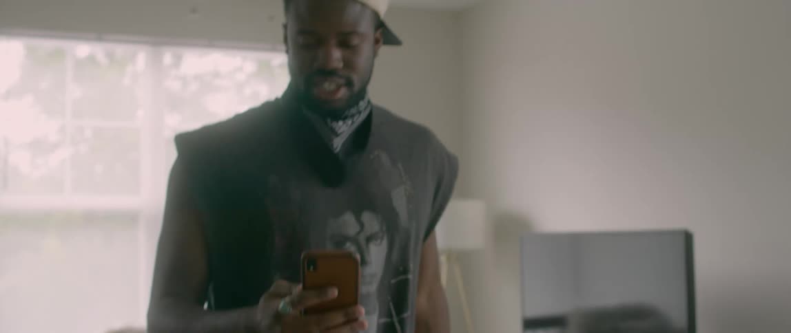 Man sitting in front of laptop stands up while making a video call on smartphone