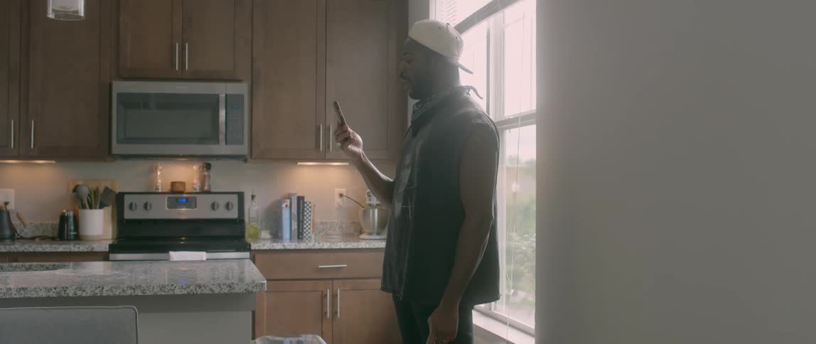 A black man stands in a kitchen and talks on a smartphone