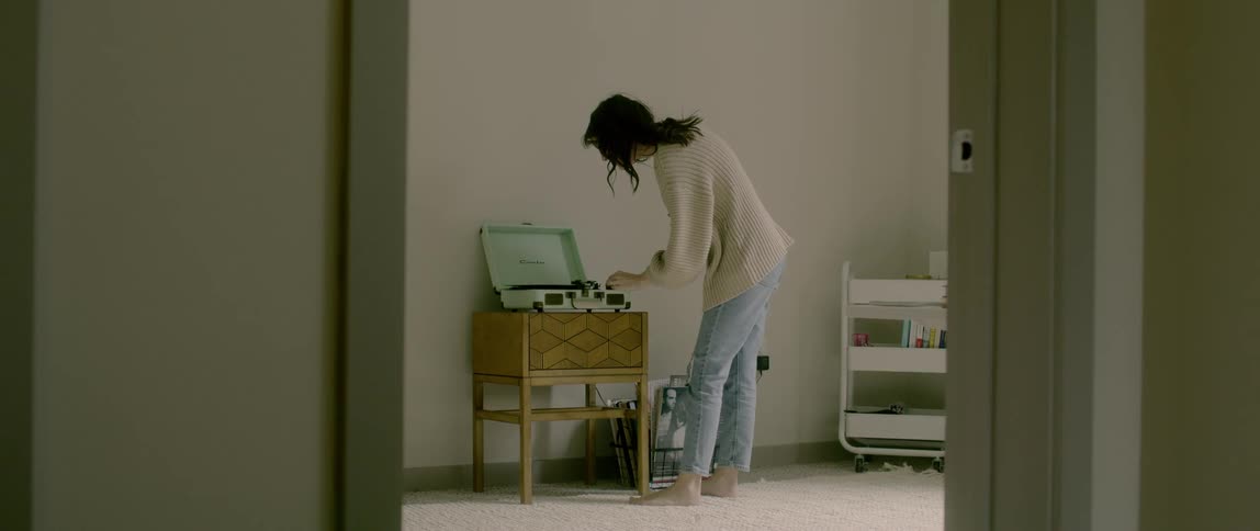 A woman stands in a bedroom and chooses a record to play