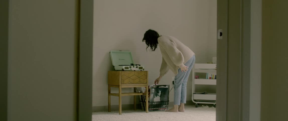 A woman walks into a room and picks out a record from a rack