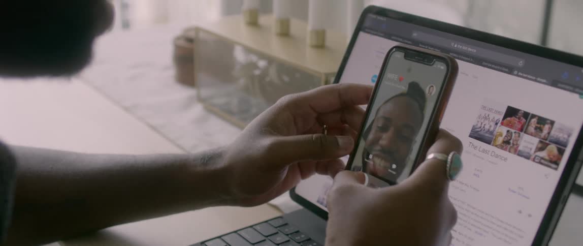 A man working on his laptop picks up his cellphone when it rings and video chats with a woman