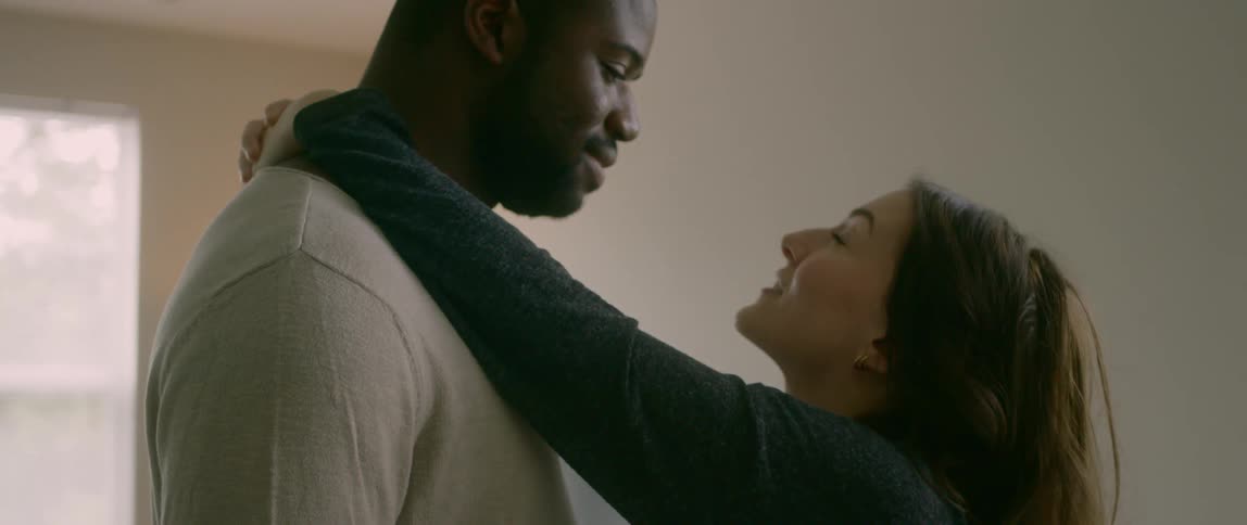 Couple slow dance near window under white ceiling fan