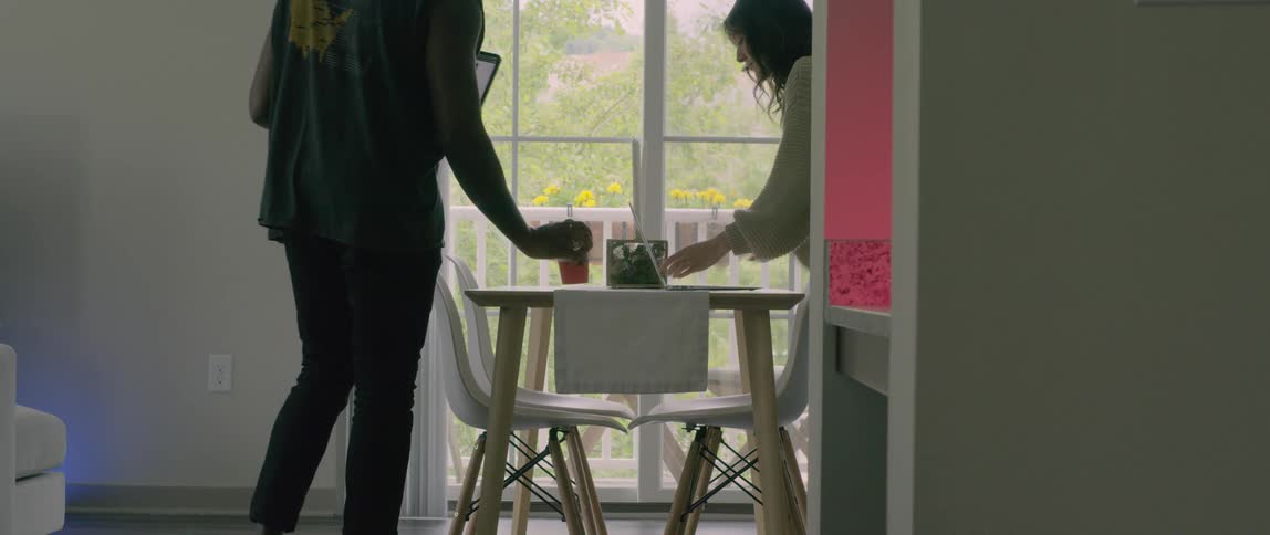Couple sits down in table on living room with laptops
