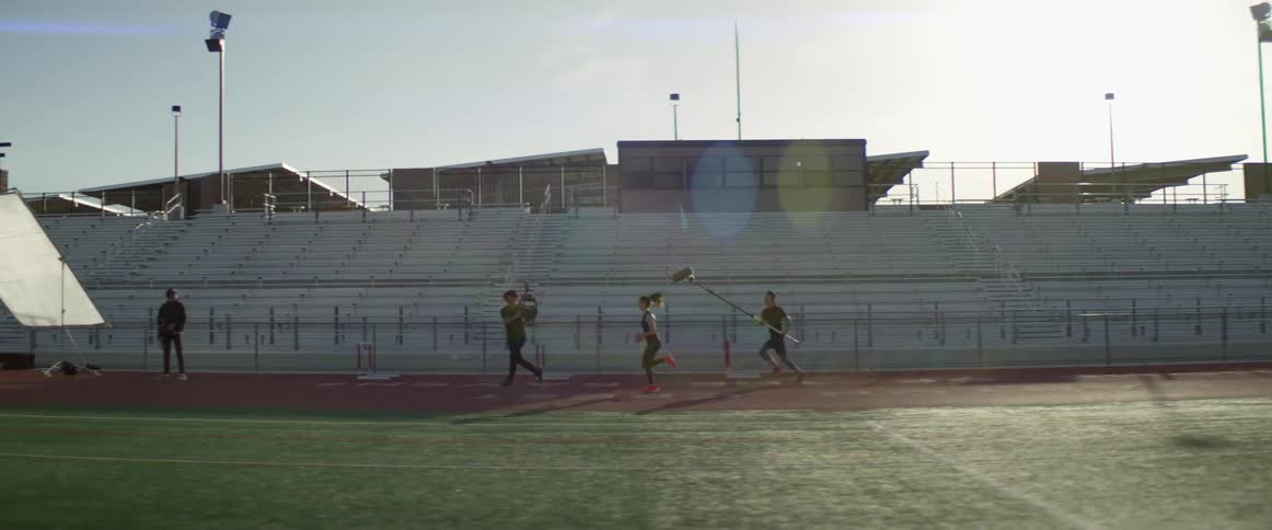 A camera crew photographs a pole vaulter running on a track