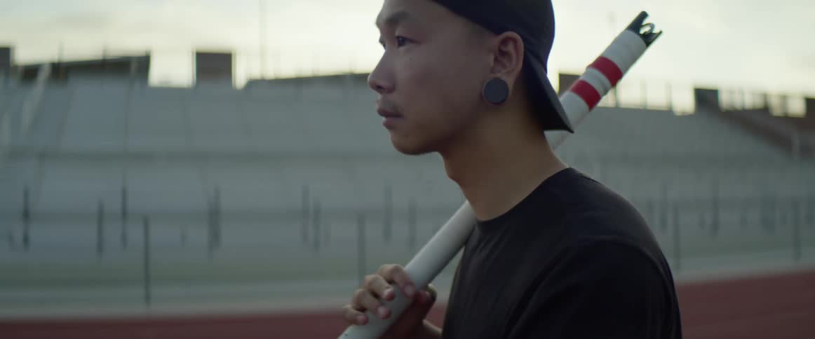 An asian man holds a pole in a stadium and looks off into the distance