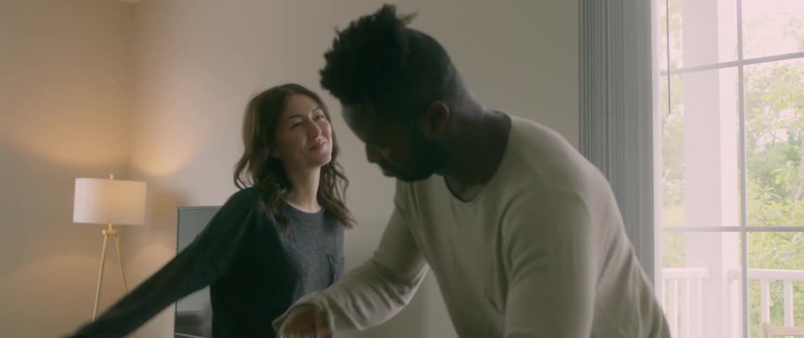 A man and woman dance around their living room together laughing