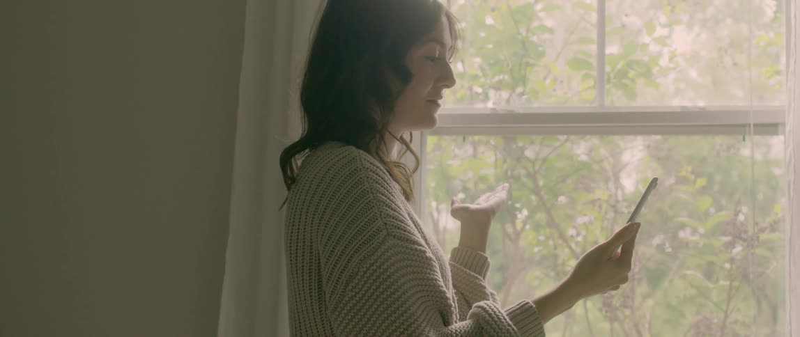 A woman is looking out a window and talking on a cellphone