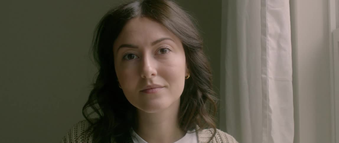 A woman standing inside by a woman looks deep in thought and then smiles
