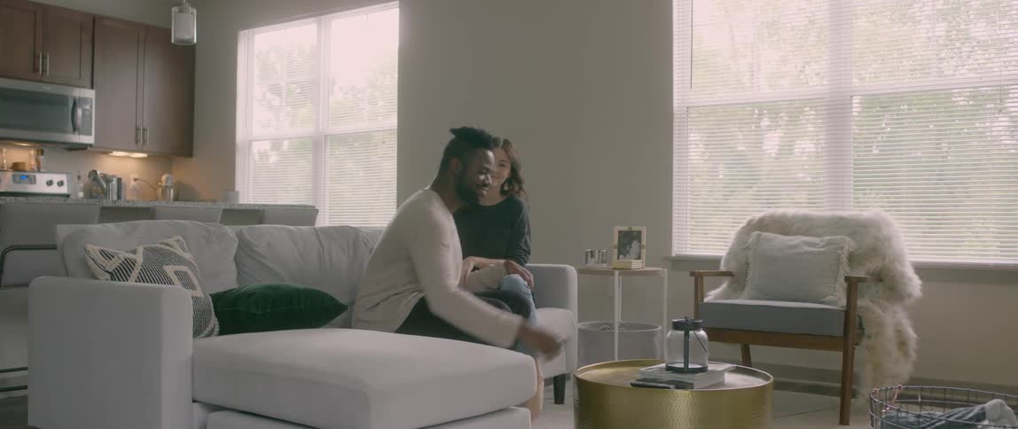 A black man and an asian woman sit in a living room and talk